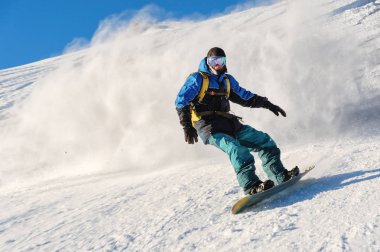 Freeride snowboard kar toz mavi gökyüzüne karşı geride bırakarak bir karla kaplı yamaç rulo