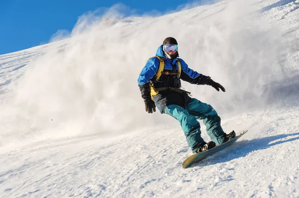 Фрірайд сноубордист катається на засніженому схилі, залишаючи за собою сніговий порох на блакитному небі — стокове фото