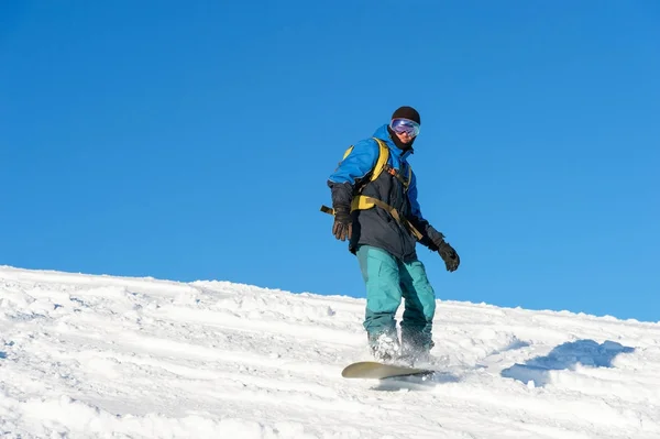 Freeride snowboarder ρολά σε μια πλαγιά χιονισμένη αφήνοντας πίσω μια σκόνη χιόνι ενάντια στον γαλάζιο ουρανό — Φωτογραφία Αρχείου