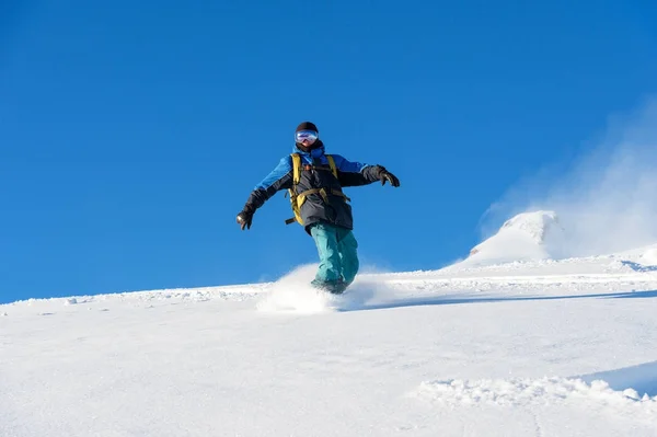 Freeride snowboarder rueda sobre una pendiente cubierta de nieve dejando un polvo de nieve contra el cielo azul — Foto de Stock