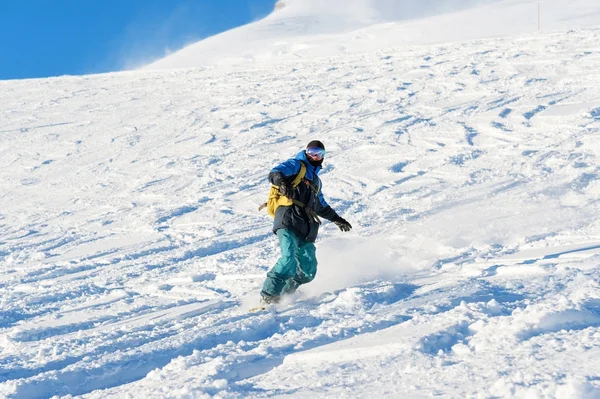 Freeride-Snowboarder rollt auf einer schneebedeckten Piste und hinterlässt einen Schneepuder gegen den blauen Himmel — Stockfoto