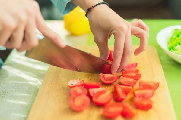 Hands of a young girl chop the cherry tomatoes on a wooden cutting board on a green table in a home setting — Stock Photo, Image