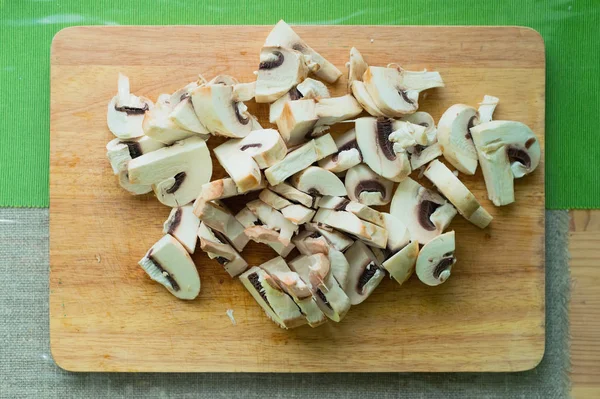 Primer plano de los champiñones picados acostados en una tabla de cortar de madera sobre una mesa de cocina verde . — Foto de Stock