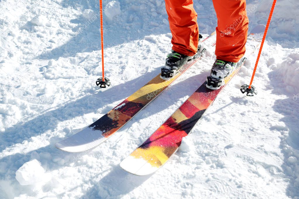 Legs athlete skier in an orange overall on a sport skiing on snow on a sunny day. The concept of winter sports