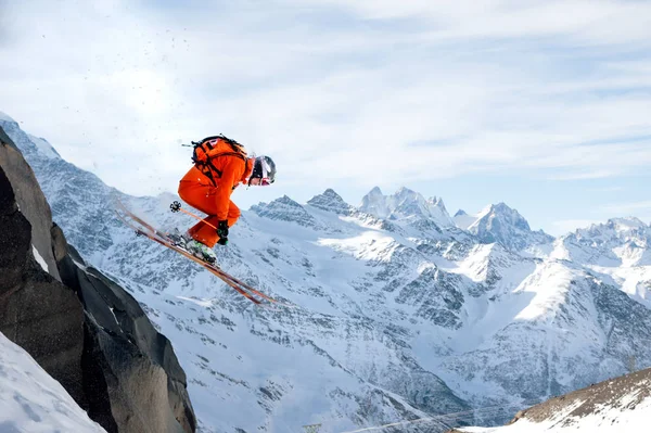 Ein professioneller Skifahrer macht einen Sprung von einer hohen Klippe vor blauem Himmel und hinterlässt eine Spur von Schneepuder in den Bergen — Stockfoto