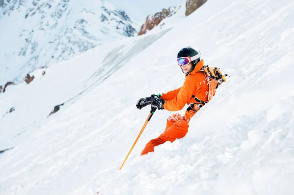 Ein Skifahrer in orangefarbenem Overall und mit Rucksack sitzt nach dem Sturz glücklich im Schnee. — Stockfoto