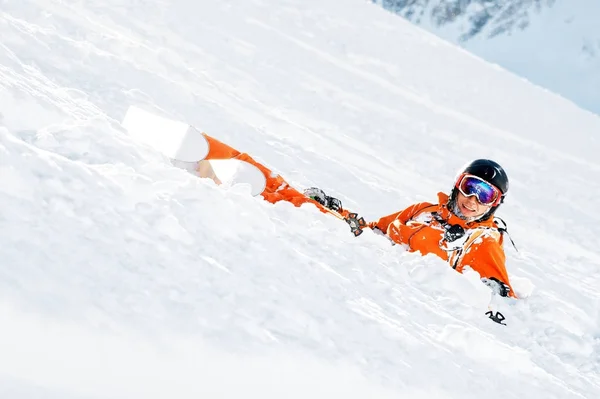 Lyžař v pomeranč celkově a s batohem leží šťastný ve sněhu po pádu. — Stock fotografie
