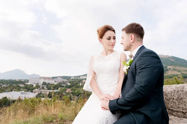Milující pár novomanželé sedí na pozadí panoramatu malé letovisko na Kavkaze. Nově vdaná něžně hladit navzájem — Stock fotografie