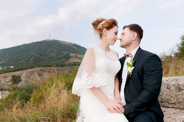 A loving couple of newlyweds sits on the background of the cityscape of a small resort town in the Caucasus. Newly married gently caress each other