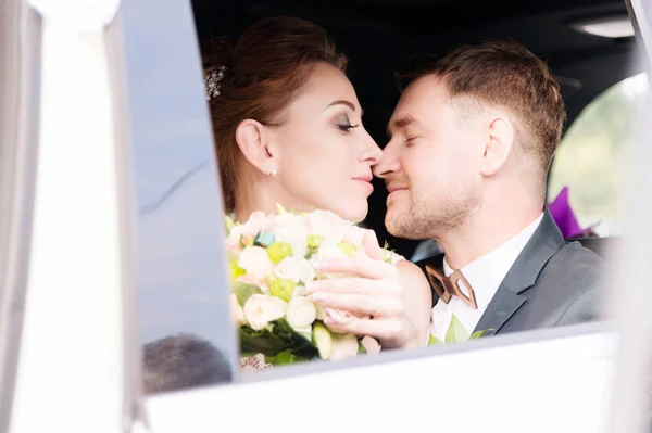 Porträt eines jungen küssenden Paares, das sich in ein frisch vermähltes Paar verliebt, neben einem Strauß im Fenster eines Hochzeitswagens. — Stockfoto