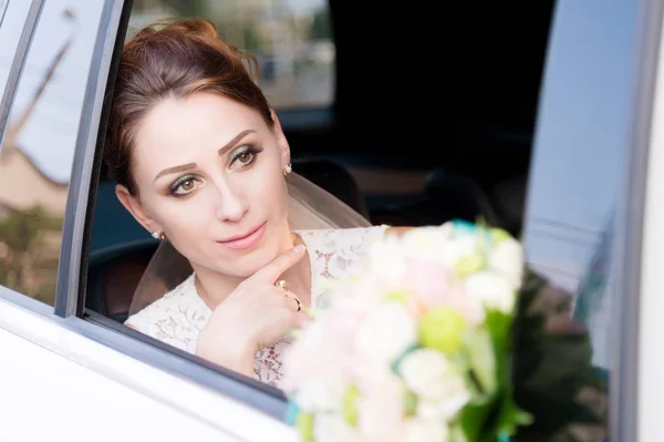 Close-up portrait of a beautiful bride aged beside her wedding bouquet in the window of a wedding car. — Stock Photo, Image
