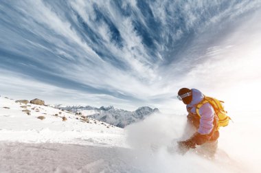 Epik bulutlar ve koyu mavi gökyüzü arka plan üzerinde günbatımında karlı toz bulutu bırakarak bir sırt çantası ile profesyonel snowboarder