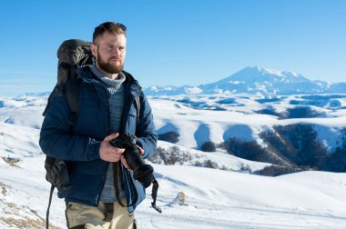 Hipster fotoğrafçı bir sırt çantası ile portre A sakallı ve onun elinde bir Dslr fotoğraf makinesi ile güneş gözlüğü takıyor oturur