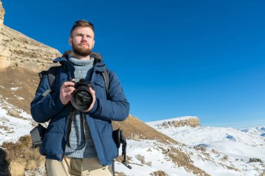 Hipster fotoğrafçı bir sırt çantası ile portre A sakallı ve epik kayalar arka planı elinde bir Dslr fotoğraf makinesi ile güneş gözlüğü takıyor duruyor