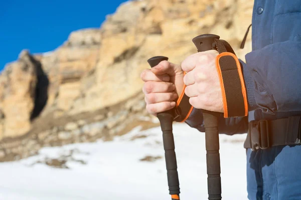 壮大な岩の麓に雪背景にノルディック ・ ウォーキング用スティックと立っている肖像画はひげを生やしたヒップスター バックパックと彼の肩に大きなバックパックとサングラス. — ストック写真