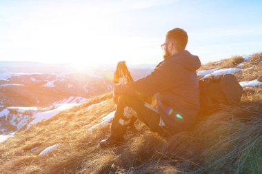 Kış karla kaplı dales çerçevede bir hipster seyahat sakal ve güneş gözlüğü ile sarı bir çim üzerinde bir eğriltme oturur