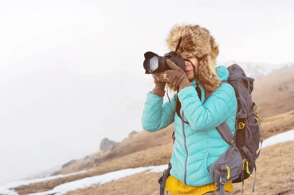 Portrét dívky sladké turistické ve velké kožešinovou čepici se fotí na její digitální fotoaparát v horách. — Stock fotografie