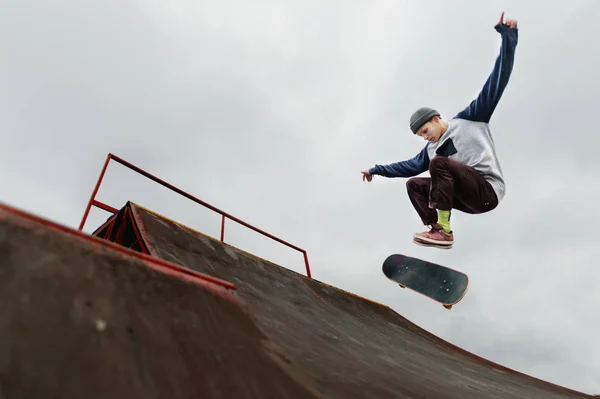 Teenager skateboardista v čepici dělá trik skok na rampě na pozadí zamračená obloha — Stock fotografie