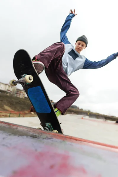Підліток скейтбордист в капелюсі робить трюк Скелі на пандусі в скейт-парку проти хмарного неба і спальної зони. Концепція міського стилю в спорті — стокове фото