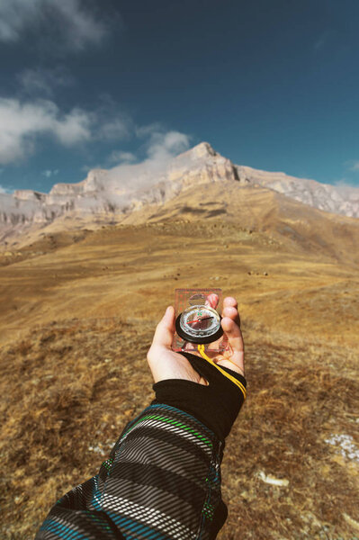Снимок со смотровой. Вид от первого лица руки человека держит компас на фоне эпического ландшафта с скалами холмов и голубое небо с облаками
