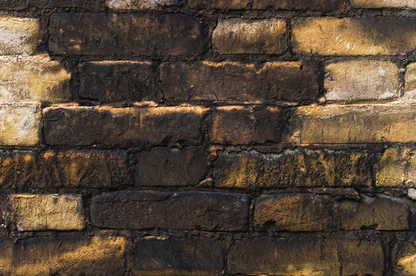Close-up Textured background of old faded bricks stained with black oil. A brick gradient between dirty black and light yellow bricks. Grunge style