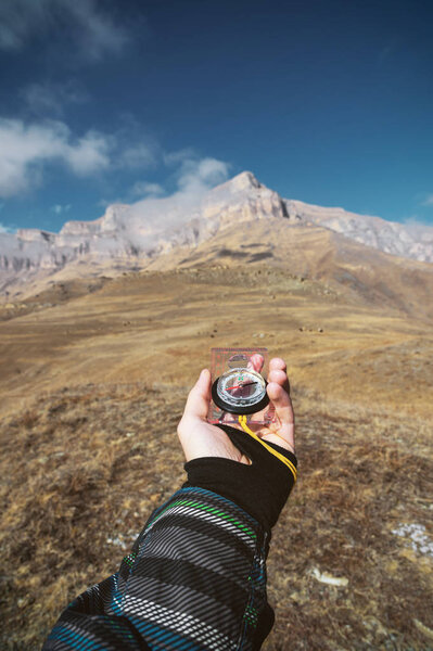 Снимок со смотровой. Вид от первого лица руки человека держит компас на фоне эпического ландшафта с скалами холмов и голубое небо с облаками
