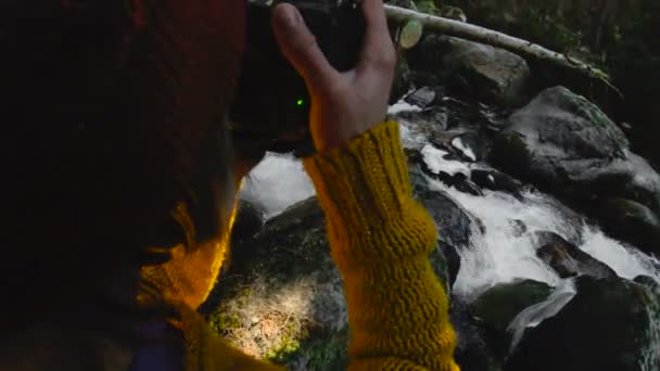 Μια ενεργή και υγιή hipster κορίτσι-φωτογράφος με μια φωτογραφική μηχανή στα χέρια της βόλτες μέσα στο δάσος. Το κορίτσι παίρνει τις εικόνες. Χαμηλό βασικό 60 Fps, αργή κίνηση. GoPro 6 Black με ένα αντιμικροβιακό τριών αξόνων — Αρχείο Βίντεο