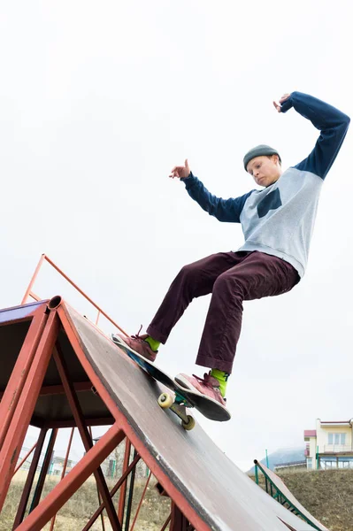 青少年选手在连帽运动衫和牛仔裤幻灯片的栏杆上踩着滑板在滑板公园 — 图库照片
