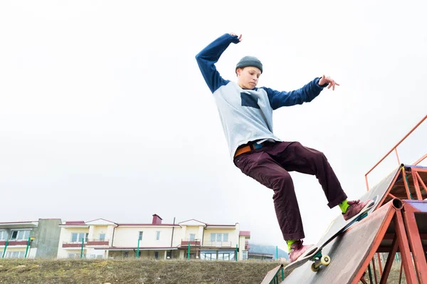 Підліток ковзаняр в светрі і джинсах ковзає по перилах на скейтборді в скейтборді парку — стокове фото