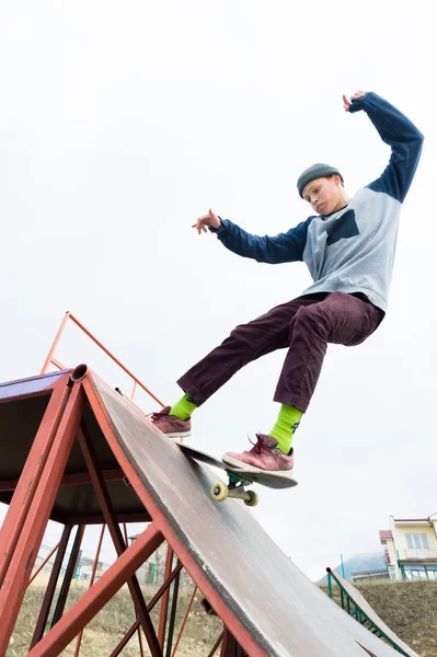 Teenager-Skater in Kapuzenpulli und Jeans rutscht auf Skateboard über Geländer in Skatepark — Stockfoto