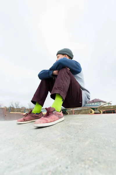 Um adolescente está sentado num skate no parque. O conceito de passatempo de tempo livre para adolescentes na cidade — Fotografia de Stock