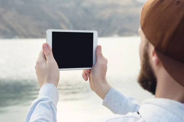 Hipster person holding in hands digital tablet with empty blank screen, man photograph on computer on background nature outdoor landscape mock up technology blur male hands tourist using gadget