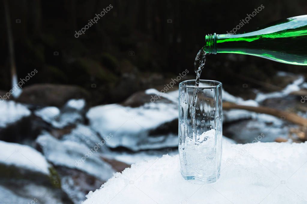 Mineral mineral water is poured from a glass green bottle into a clear glass beaker.