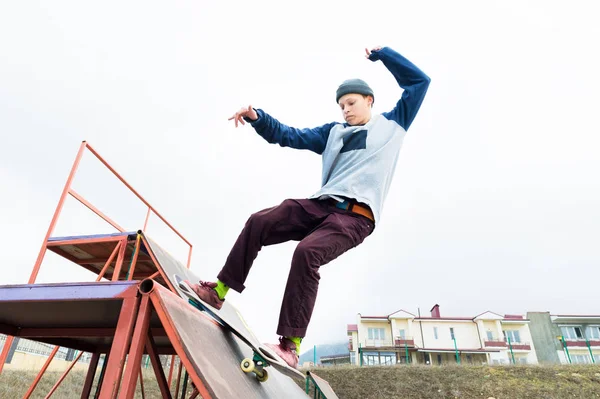 Adolescente patinador em uma camisola com capuz e jeans desliza sobre um corrimão em um skate em um parque de skate — Fotografia de Stock
