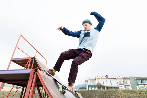 Tini korcsolyázó egy kapucnis pulóver és a farmer diák-ért, már több mint egy korlát egy gördeszka, skate park — Stock Fotó