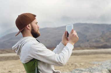 Bir kap içinde sakallı hippi ve bir kazak onun elinde bir tablet ile fotoğraf göl kenarında niteliğine olurken bir tablete çeker