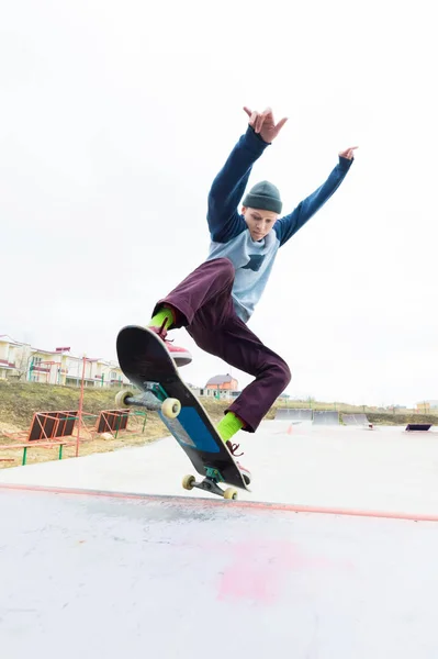 Un adolescente patinador con sombrero hace un truco con un salto en la rampa. Un patinador vuela en el aire — Foto de Stock