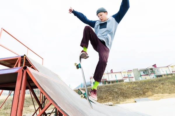 Ein Skateboarder-Teenager mit Hut macht einen Trick mit einem Sprung auf die Rampe. Ein Skateboarder fliegt in die Luft — Stockfoto
