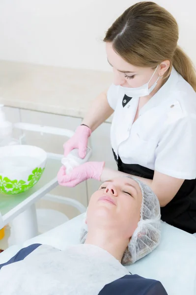 Il cosmetologo prende in mano un detergente per la pulizia a umido del viso della ragazza sdraiata sul divano. Il concetto di cosmetologi lavora in una sala cosmetologica professionale — Foto Stock