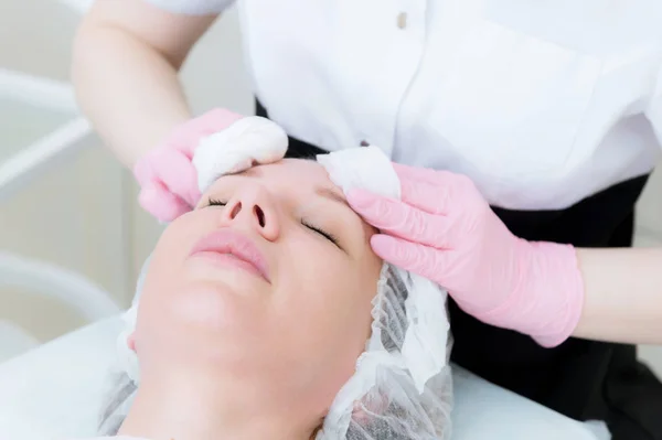 Un primer plano del procedimiento de limpieza en la oficina de cosmetología. Las manos del cosmetólogo en guantes rosados se retiran de la cara de una joven con una esponja limpiando la máscara — Foto de Stock