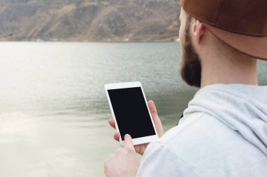 Açık havada kahverengi şapkalı bir kalabalık Close-Up beyaz tablet pc elinde tutar. Sakallı bir adam tablet vasıl görünüyor. OTS görünümü omuz arkasından. Bir takas parmağıyla hareket yapar