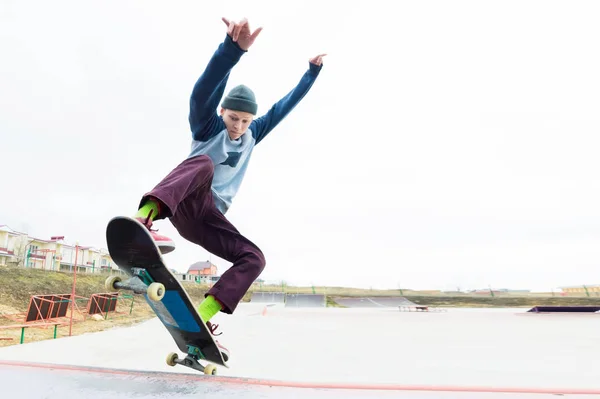一个戴着帽子的滑板少年在坡道上跳上了一招。滑板在空中飞翔 — 图库照片