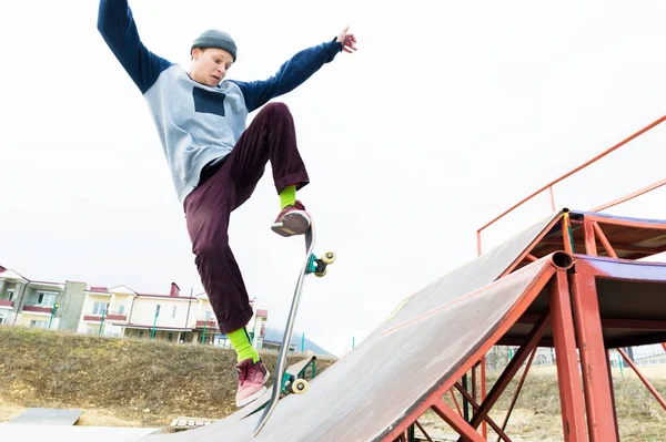 Um adolescente skatista de chapéu faz um truque com um salto na rampa. Um skatista está voando no ar — Fotografia de Stock