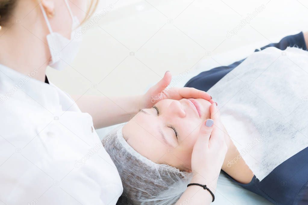 Beauty saloon. Close-up of a medical beautician in pink gloves makes a face massage of a beautiful woman. Cosmetology. Head and shoulders of a girl with closed eyes. The concept of womens beauty and