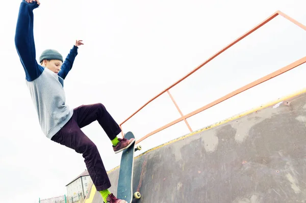 Adolescente patinador em uma camisola com capuz e jeans desliza sobre um corrimão em um skate em um parque de skate — Fotografia de Stock