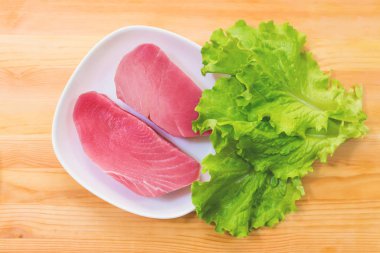 Ham taze ton balığı filetosu bir plaka üzerinde iki adet büyük yeşil salata yaprakları üzerinde ahşap bir masa ile. Lezzetli deniz ürünleri kolay. Yunan mutfağı