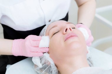 Bir close-up kozmetik ofis temizlik yordamı. Güzellik uzmanı pembe eldiven eller genç bir kız yüzünden maske temizlik sünger ile kaldırılır