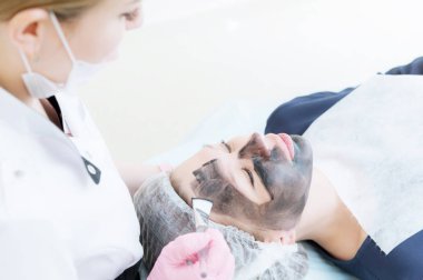 Güzellik uzmanı bir fırça ile pembe eldiven karbon maske peeling yüzünde bir kozmetik odasında genç bir kız için geçerlidir. Kozmetoloji hizmetleri ve öz bakım kavramı. Kavramı