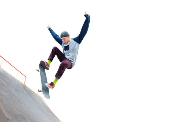 Lo skateboarder adolescente nel berretto fa un trucco con un salto sulla rampa nello skatepark. Pattinatore isolato e rampa su sfondo bianco — Foto Stock