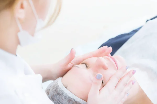 Salón de belleza. El primer plano de la esteticista médica en los guantes rosados hace el masaje facial de la mujer hermosa. Cosmetología. Cabeza y hombros de una chica con los ojos cerrados. El concepto de belleza de las mujeres y — Foto de Stock